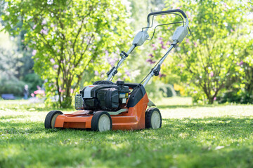 Fototapeta na wymiar Electric lawn mower for cutting grass on courtyard in private house in summer. Gardening, working in garden. Obligation of home owners to mow lawns concept. Maintenance cleaning of house territory.