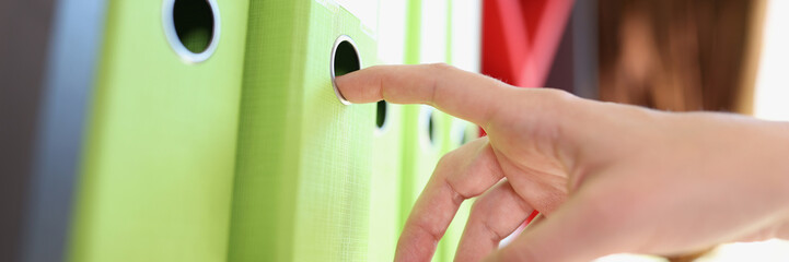 Female manager takes one folder with documents from shelf in the office close-up.