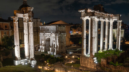 Three Roman ruins illuminated in white light at night in the Roman Forum. Ruins of the Temple of...