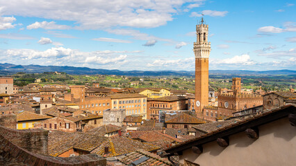 Fototapeta na wymiar Daytime cityscape view of the Tuscan town of Siena, Italy. View as seen from the top of the Duomo di Siena cathedral, with the Torre del Mangia tower prominent on the right side of the frame.