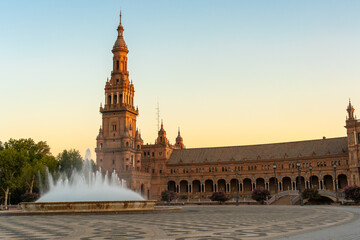 Naklejka premium Daytime landscape image of the Plaza de Espana in Seville, Spain. Part of the building is lit with golden sunrise light, and a fountain is flowing in front of the building.