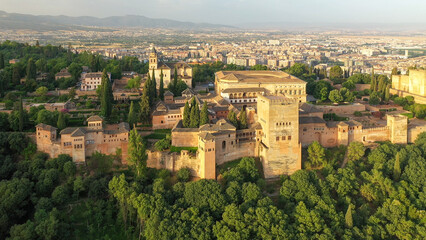 Fototapeta na wymiar Aerial sunrise image of the Alhambra fortress in Granada, Spain. The fortress is bathed in reddish-orange light with green trees interspersed among towers.
