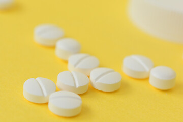 Fototapeta na wymiar 黄色い背景に、白い複数の錠剤と転がった薬のボトル