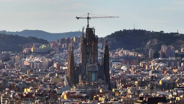 Zoomed shot of cranes on Sagrada Familia construction. Famous cathedral towering above surrounding town development. Barcelona, Spain