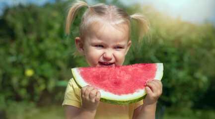 Happy child enjoys eating watermelon, makes a face outdoors in the garden. Healthy snack for children