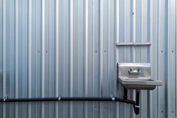 A metal sink installed on the exterior of a corrugated metal wall