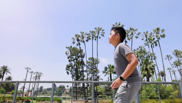 12 year old boy jogs around a park with a small lake in Los Angeles. Slow Motion.