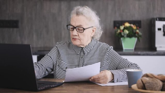 A pensioner sits at a computer in the kitchen. An elderly woman enters utility bills into her laptop. 