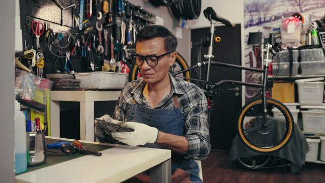 Professional senior man tightening the screw gear of bike in shop. Senior repairman fixing cog of bike wheel on table in bicycle shop. Maintenance and repair concept