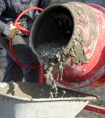 Worker pouring concrete with cement mixer at construction site, closeup