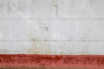 An old riveted metal plate - side of a sea vessel - painted in white with red waterline as an industrial background