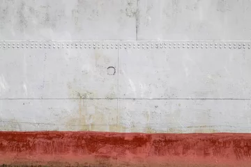 Foto op Plexiglas Schip An old riveted metal plate - side of a sea vessel - painted in white with red waterline as an industrial background