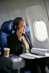 A successful Asian businesswoman talking on the phone during the flight to her business trip.