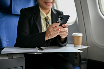 A happy senior Asian businesswoman using her smartphone during the flight