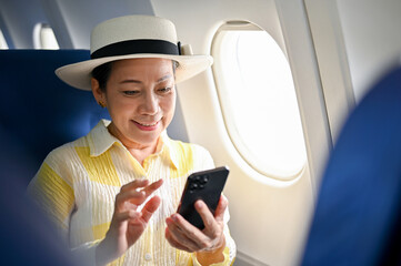 A happy senior Asian female passenger using her phone on a flight, travelling for her summer trip.