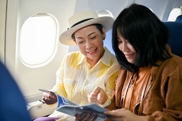 A happy Asian grandmother is reading a magazine with her granddaughter during the flight