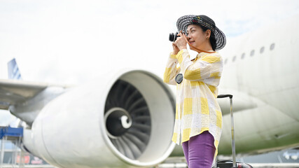 A happy senior Asian female tourist taking pictures with her film camera at the airport.