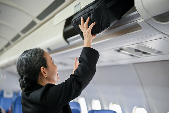 A senior female passenger is putting her luggage in an overhead locker before takeoff.