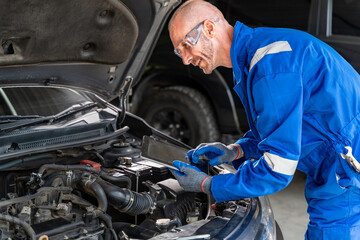 A male car mechanic using his computer tabet to check on the car's engine while working it at the...