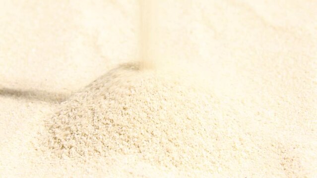 Light sand pours in a stream into a pile. Monotonous soothing, relaxing ASMR video. Grains of sand are visible in close-up.