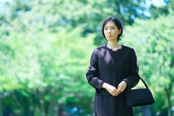 喪服姿で緑地に立つ女性