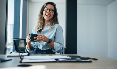 Professional business woman sitting in an office, smiling and holding a cup of coffee