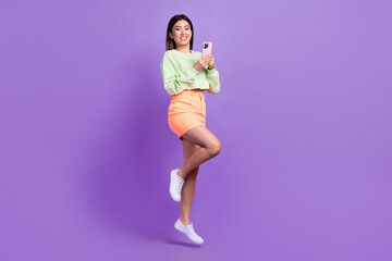 Full length photo of optimistic nice cute girl hold smartphone facebook twitter whatsapp instagram isolated on violet color background