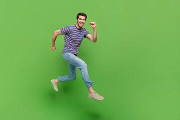 Fototapeta na wymiar Full length photo of handsome cute man dressed striped t-shirt jumping high running empty space isolated green color background