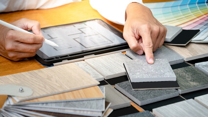 Architect hand choosing and pointing stone and wood material samples while working with digital...