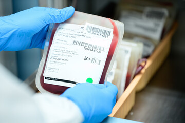 Close up scientist hand holding red blood bag in storage refrigerator at blood bank unit...
