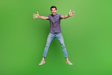 Full length photo of cheerful impressed man dressed striped t-shirt jumping high catching arms huge object isolated green color background