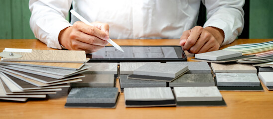 Architect hand choosing and picking stone and wood material samples while drawing on a digital...