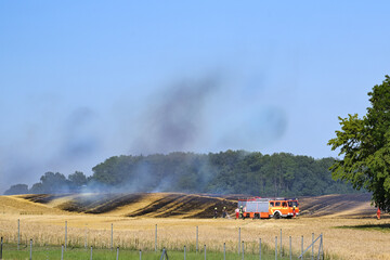 Fototapeta na wymiar Fire engine and firefighters damping down a field fire to protect the surrounding area in a rural landscape, copy space