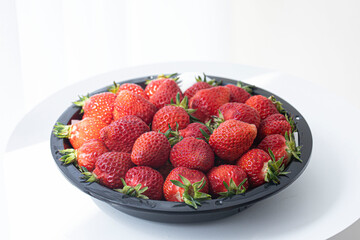 Fresh strawberry packed in black plastic bowl.