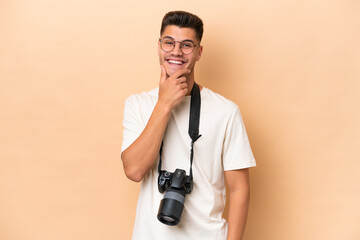 Young photographer caucasian man isolated on beige background with glasses and smiling