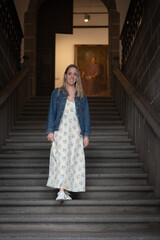 young girl in long dress and jean jacket walking down the stone steps of the luxurious manor house