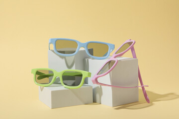 Colorful sunglasses on white blocks on beige background