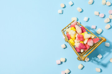 Jelly candies in shopping trolley on blue background, space for text