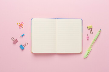 Open notebook with stationery on color background, top view