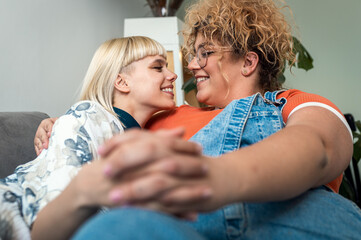 Portrait of a smiling lesbian couple sitting on sofa at home, embracing each other.