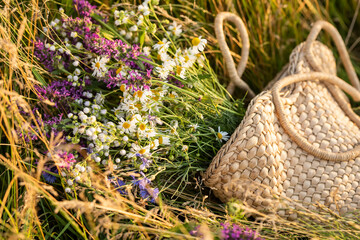 A wicker bag made of straw and a bouquet of wildflowers in the grass. Summer holiday mood.