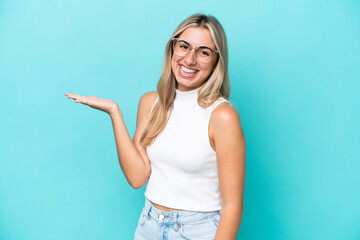 Fototapeta premium Young caucasian woman isolated on blue background holding copyspace imaginary on the palm to insert an ad