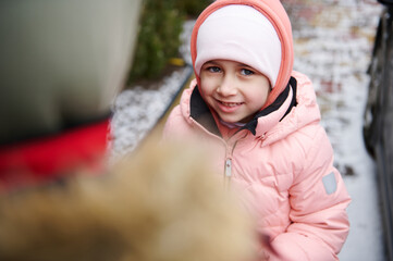 Caucasian lovely little child girl smiling looking at camera, standing near her older brother in a snow covered backyard