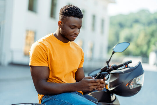Calm african american man using mobile phone at the street after motorbike riding