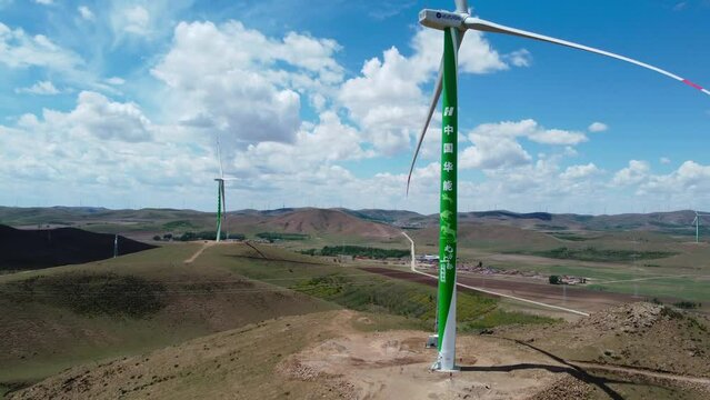 Green wind turbine standing on a meadow with other windmills. Ascending drone aerial shot.