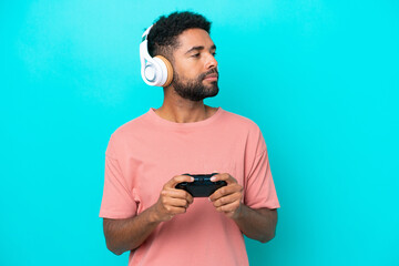 Young brazilian man playing with a video game controller isolated on blue background looking to the...