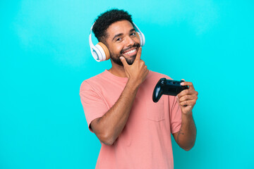 Young brazilian man playing with a video game controller isolated on blue background happy and smiling © luismolinero
