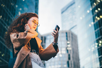 Successful woman using smartphone outdoors while standing near skyscraper at night.