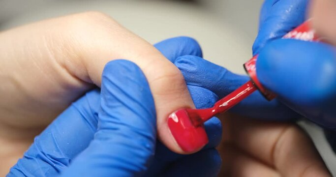 Manicurist applies red lacquer on a woman's finger, close-up. Manicure correction, cosmetic procedure