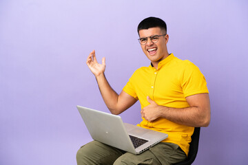 Young man sitting on a chair with laptop making guitar gesture